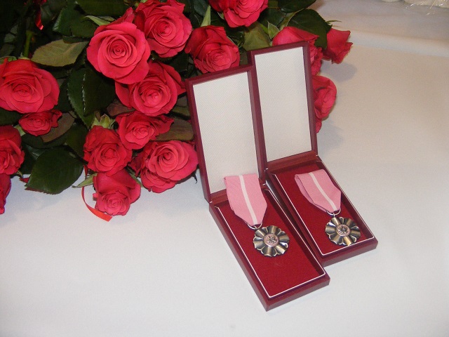 dwa medale na tle bukietu czerwonych róż